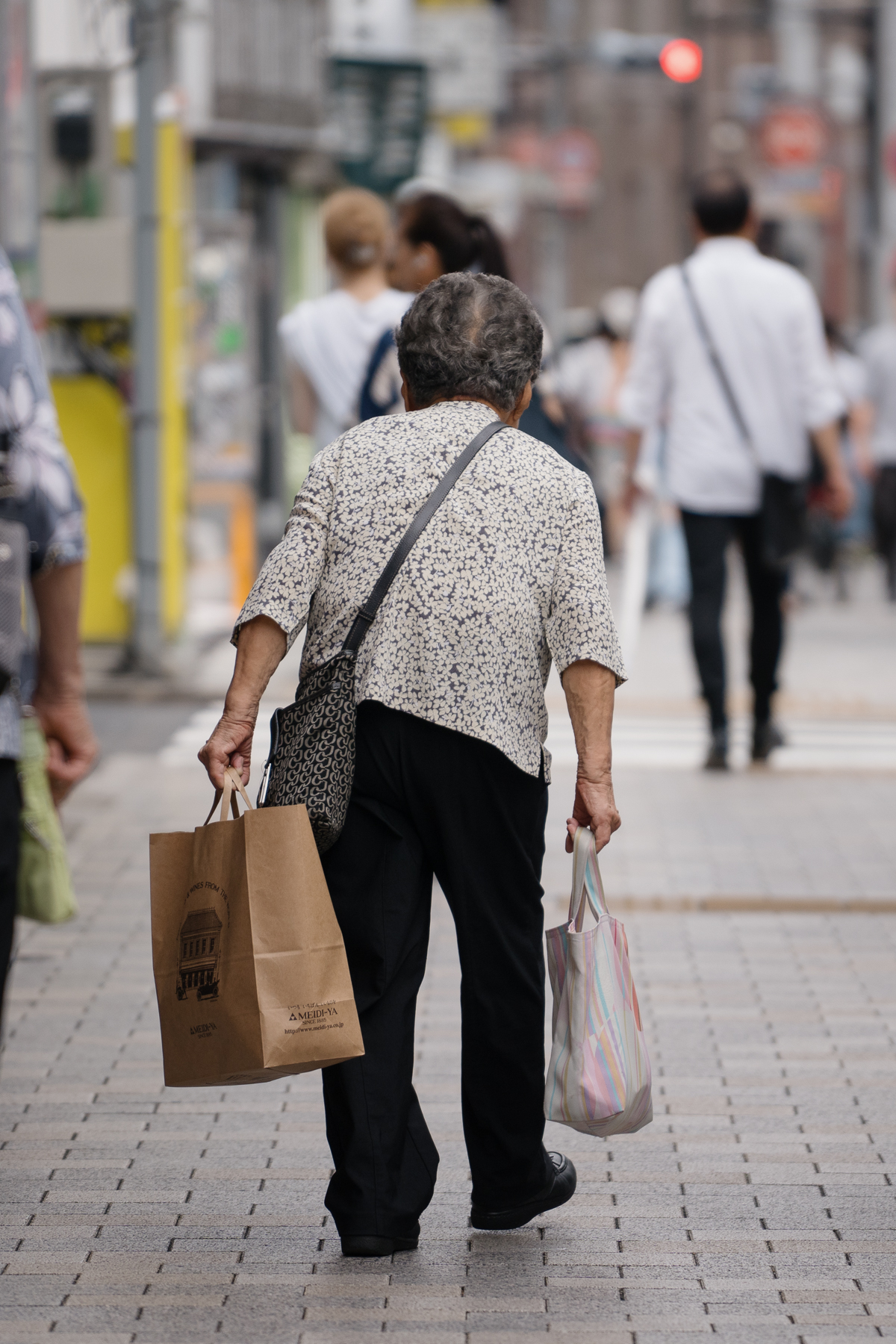<span style="color: rgb(0, 0, 0);">An elderly woman carrying multiple bags on her own. Being self-reliant is valued by both young and old.</span>