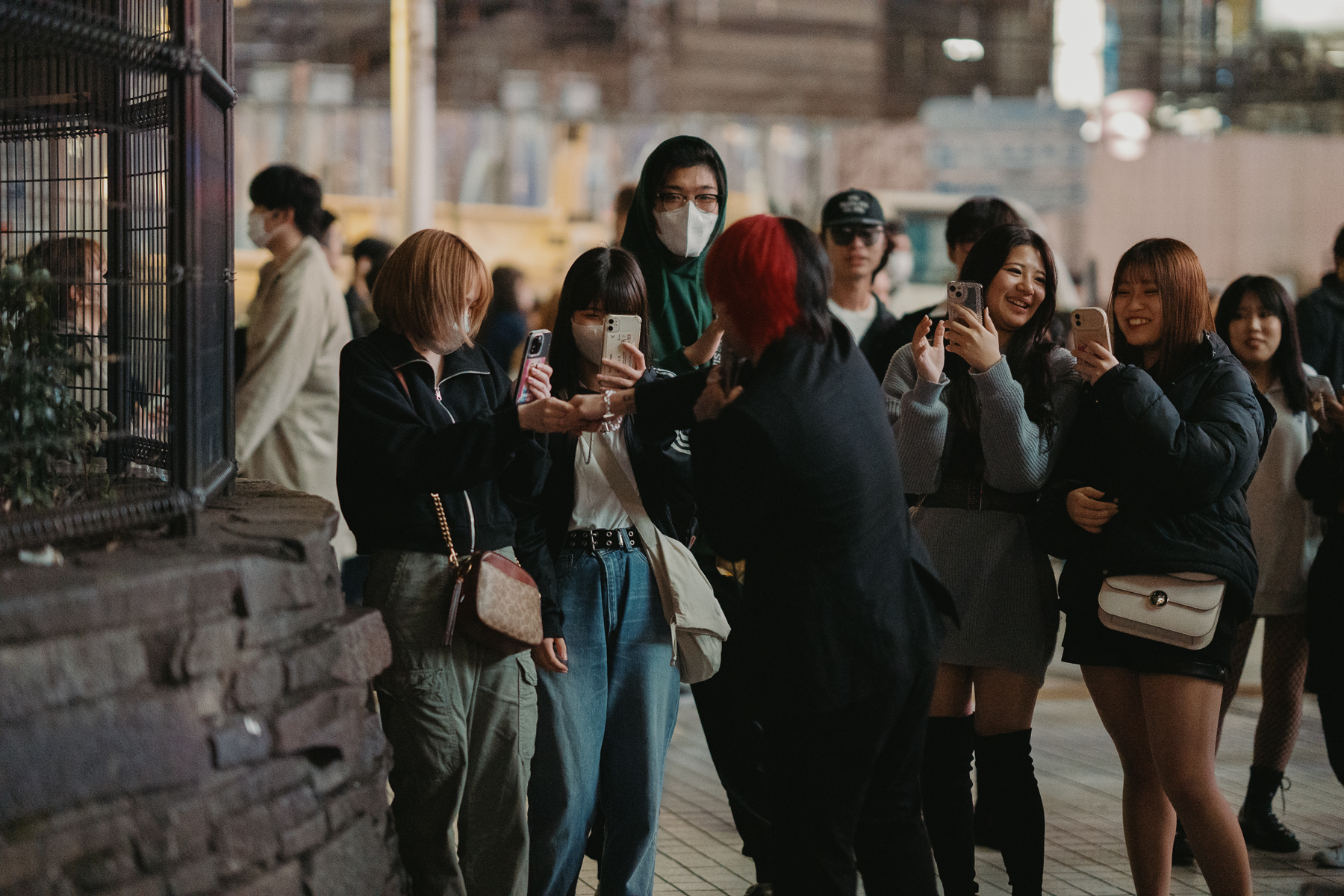 <span style="color: rgb(0, 0, 0);">Young adults recording a musician busking in Shibuya on their phones.</span>
